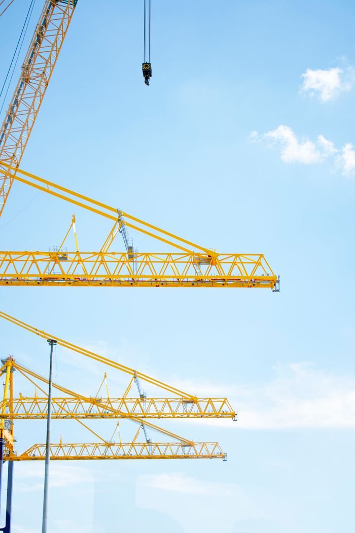 Yellow tower cranes in a construction site reaching into a clear blue sky, symbolizing modern industry.