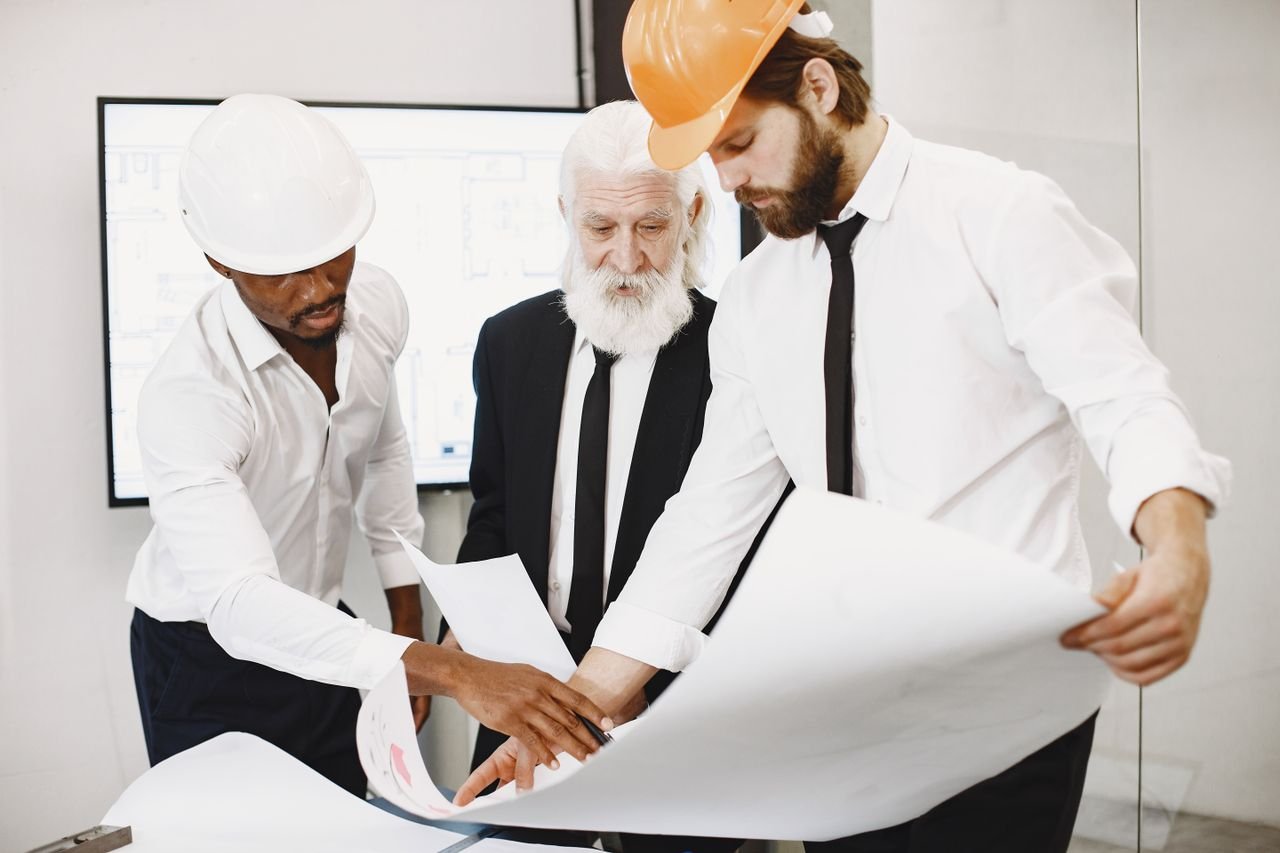 Three architects in office reviewing blueprints, showcasing teamwork and professional attire.